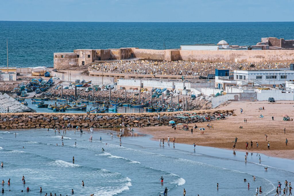 Aerial capture of a lively beach with people enjoying the waves near a historical fortress.