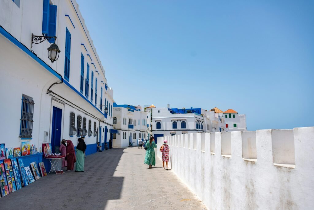 Tourists explore the scenic white and blue streets of Asilah, Morocco on a sunny day.