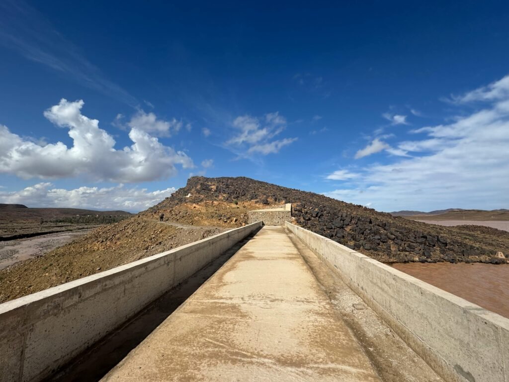 Concrete path extends towards a rocky hill surrounded by a clear blue sky and sparse desert landscape.