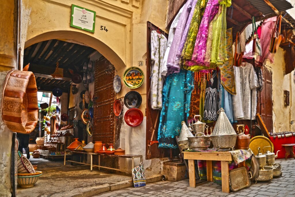 Explore the vibrant streets of Fès with traditional crafts and textiles on display in a bustling market.