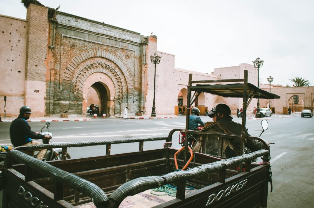 A bustling city street with motorbikes and cars near an ornate historical gate.